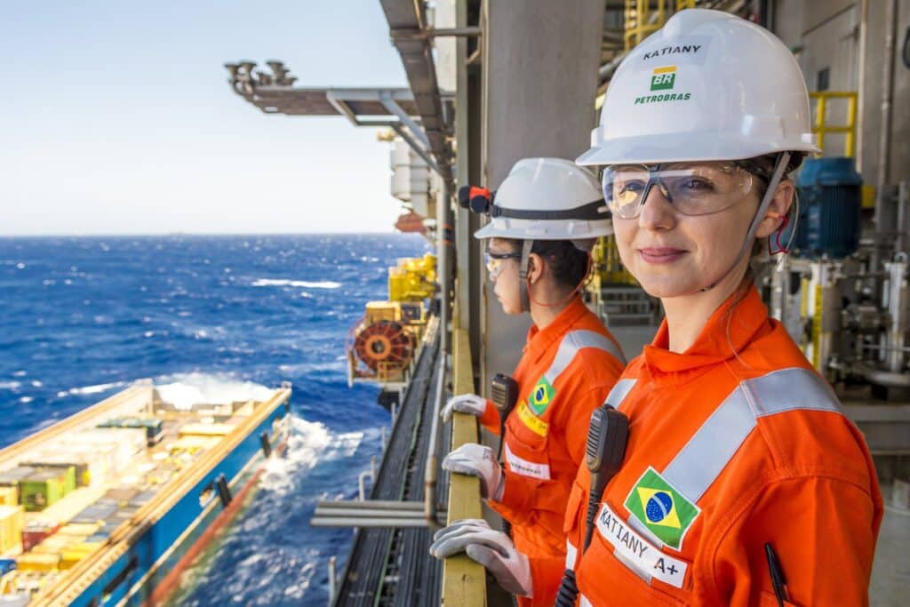 Engenheira da Petrobras trabalhando em plataforma offshore no mar com uniforme laranja e capacete de segurança