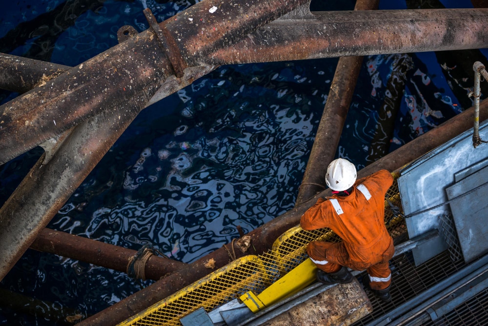 Engenheiro trabalhando em plataforma offshore da Petrobras com equipamentos industriais e oceano ao fundo