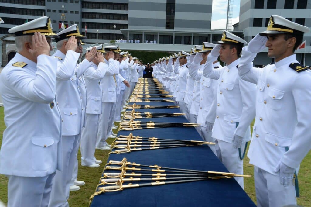 Oficiais da Marinha do Brasil em cerimônia de formatura SMV com uniformes brancos e espadas, representando carreira de oficial temporário com salário de R$ 14.240