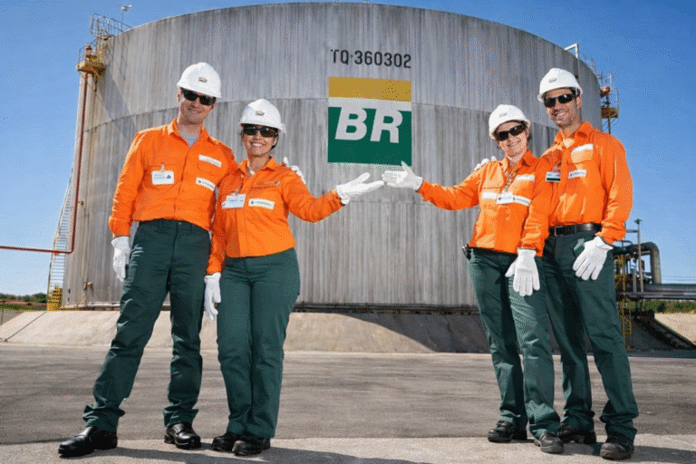 Equipe de engenheiros da Petrobras em uniforme laranja celebrando em frente a tanque de armazenamento, representando as oportunidades de vagas no concurso Petrobras 2026
