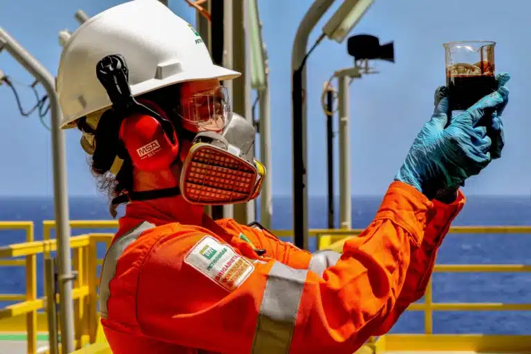 Profissional da Petrobras em plataforma offshore realizando análise laboratorial com equipamentos de proteção individual completos