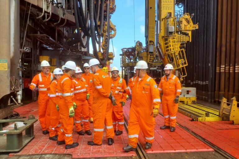 Equipe técnica da Petrobras reunida em plataforma offshore com uniformes de segurança e capacetes ao lado de equipamentos industriais