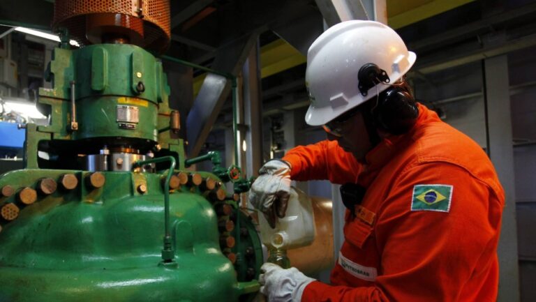 Técnico de operação da Petrobras realizando manutenção em equipamento industrial em plataforma com uniforme de segurança e capacete