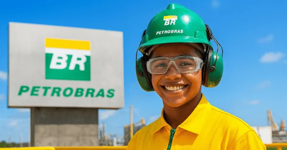 Empregada da Petrobras sorrindo com EPIs ao lado de placa com logo BR