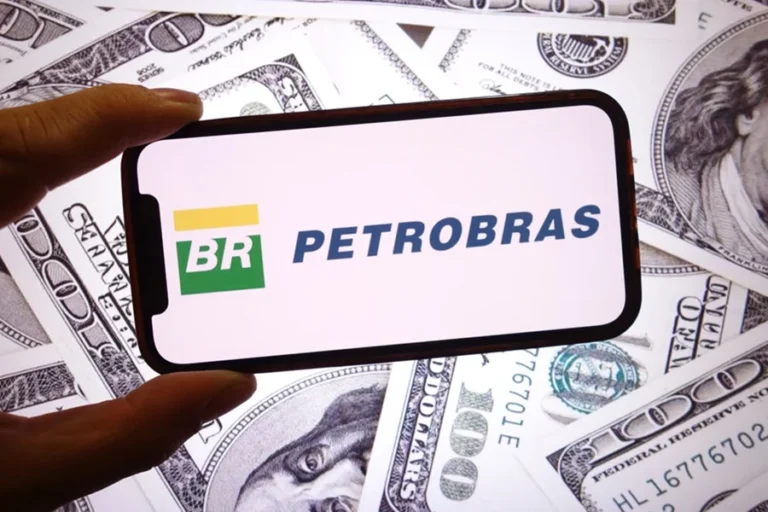 Logo da Petrobras em tela de celular sobre cédulas de dólares espalhadas