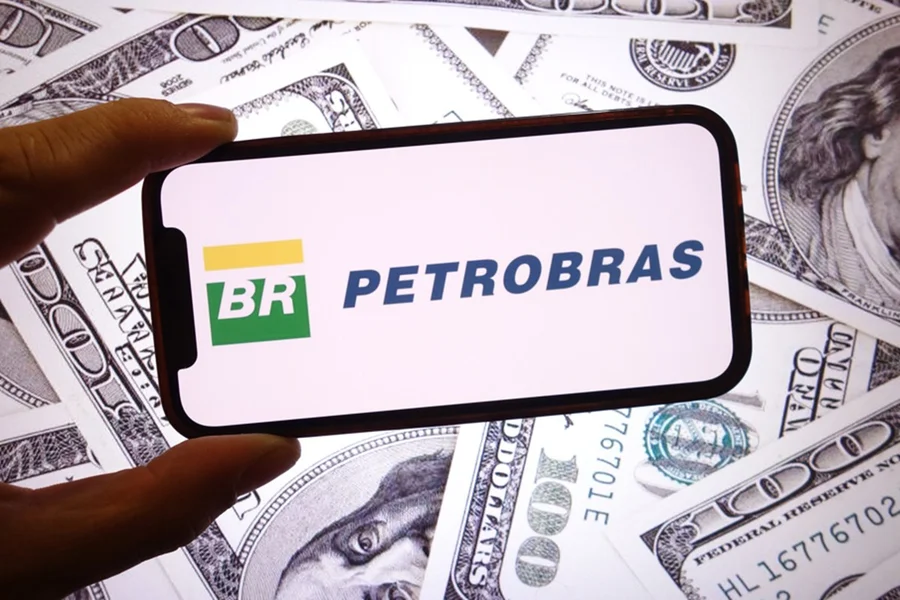 Logo da Petrobras em tela de celular sobre cédulas de dólares espalhadas