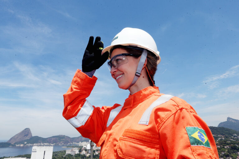 Mulher empregada da Petrobras com EPIs e vista do Rio de Janeiro ao fundo